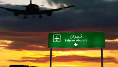 Airplane landing in Tehran with a sunset backdrop and an airport direction sign